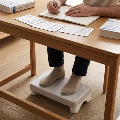Repose pieds bureau Personne écrivant à un bureau avec des fiches et des livres, les pieds posés sur un repose-pieds ergonomique blanc