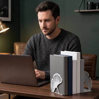 Serre livre Homme travaillant sur un ordinateur portable, avec des livres maintenus par des serre-livres décoratifs sur un bureau en bois