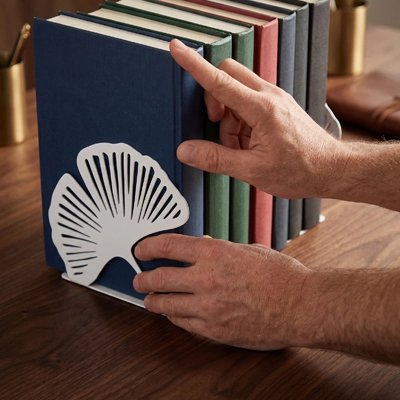 Serre livre Mains rangeant des livres maintenus par un serre-livres décoratif blanc en forme de feuille sur une table en bois
