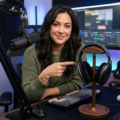 Support casque​ Femme présentant un casque audio posé sur un support de bureau en bois, dans un studio avec microphone, écran et clavier