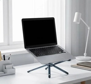 Support pliable pour ordinateur portable avec laptop surélevé sur un bureau blanc, près d’une lampe et de fournitures.