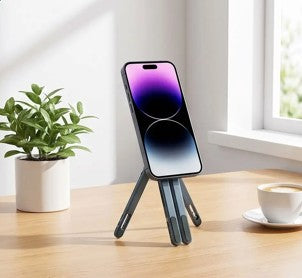 Support pliable pour téléphone avec smartphone posé sur une table en bois, près d’une plante et d’une tasse de café.