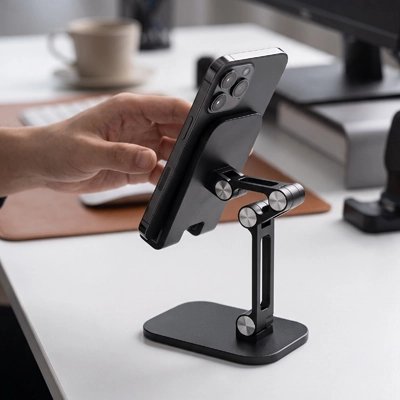 Support pour tablette Main ajustant un smartphone sur un support de bureau noir réglable et articulé, posé près de livres et d’une tasse